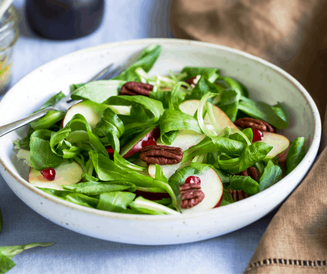Green Salad topped with pecans and apples in white bowl