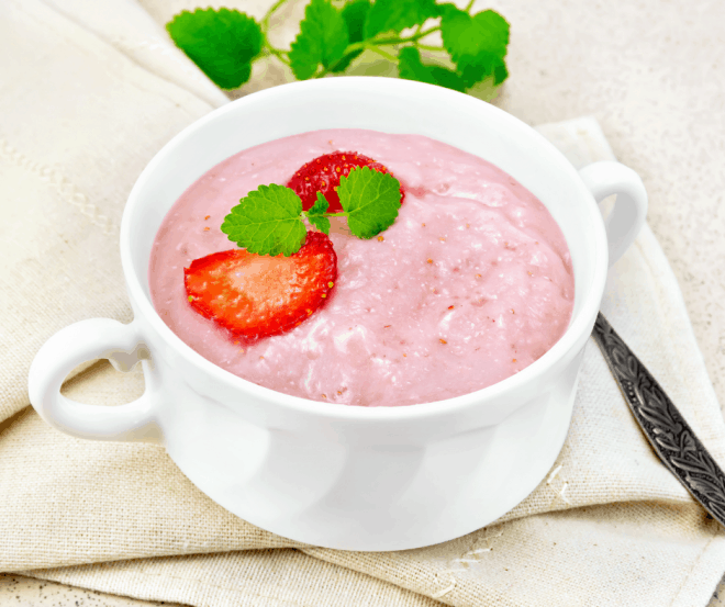 Strawberry Soup in a white bowl and garnished with mint leaves and sliced strawberries