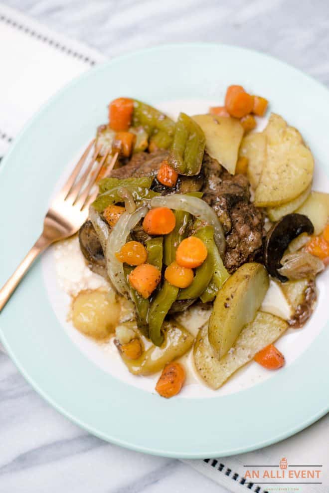 Hamburger covered with veggies and served on a white and blue plate