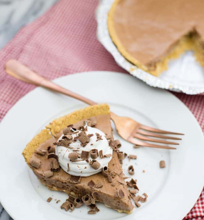 candy bar pie slice on white plate with the whole pie behind it