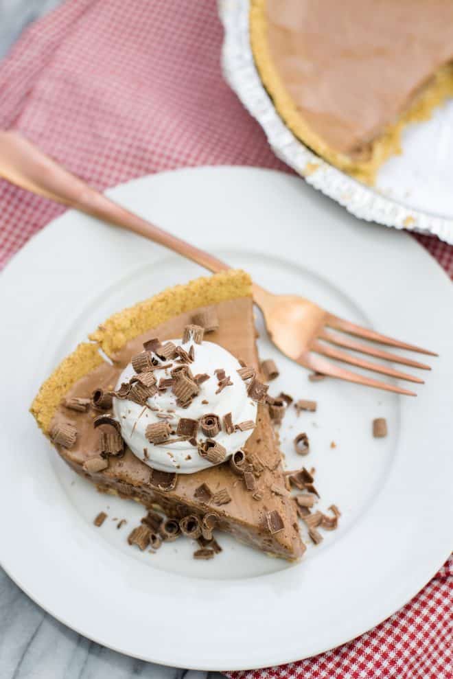 Whipped Chocolate Pie slice on white plate topped with whipped cream and chocolate curls