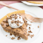 A serving of candy bar pie on a white plate with a fork sitting on a red checked napkin