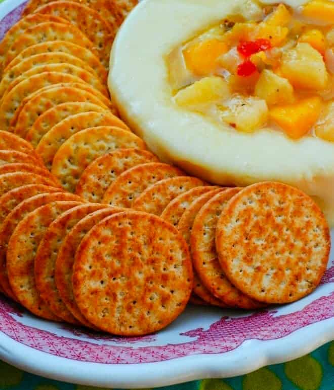 Baked Round Brie topped with a hot pepper jelly and peach topping, in a platter surrounded by round crackers