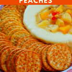 brie cheese topped with peaches and hot pepper jelly on a platter surrounded by crackers