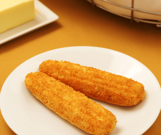 Two Cornbread Sticks On White Serving Plate With Stick of Butter in the background