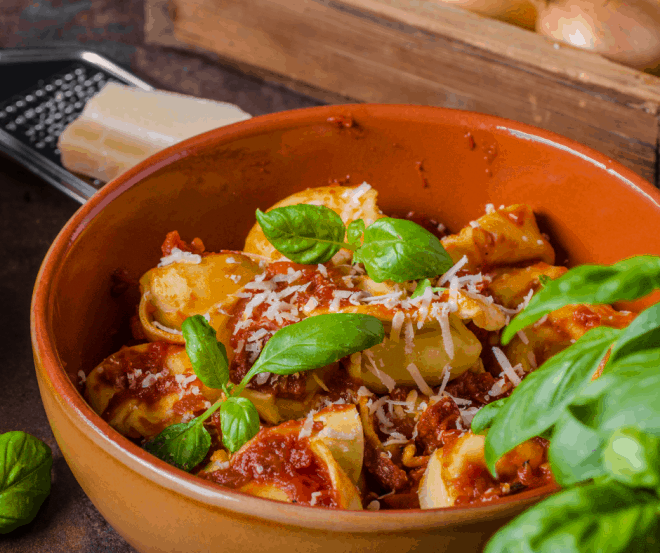 Closeup Photo of Brown bowl filled with tortellini covered in a red cheese sauce