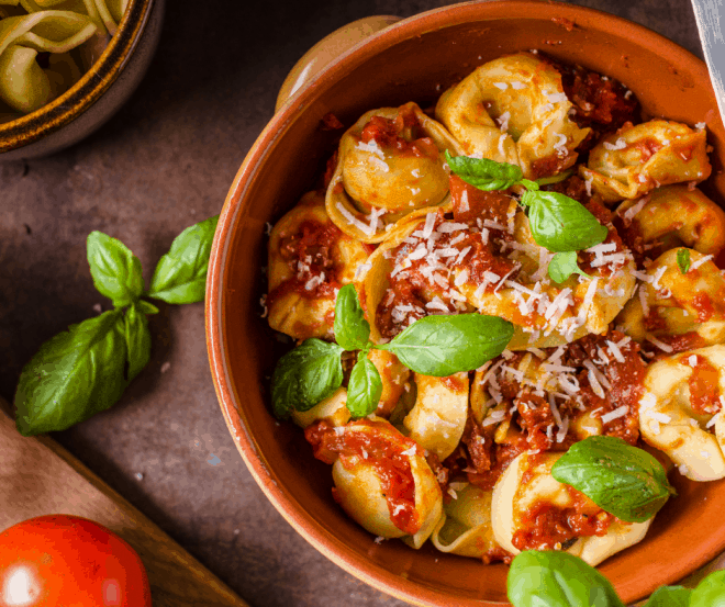 Spinach Tortellini in a brown bowl with red sauce and garnished with basil leaves