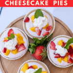 Four mini mango strawberry cheesecake pies on wooden cake plate and garnished with whipped cream and mint leaves