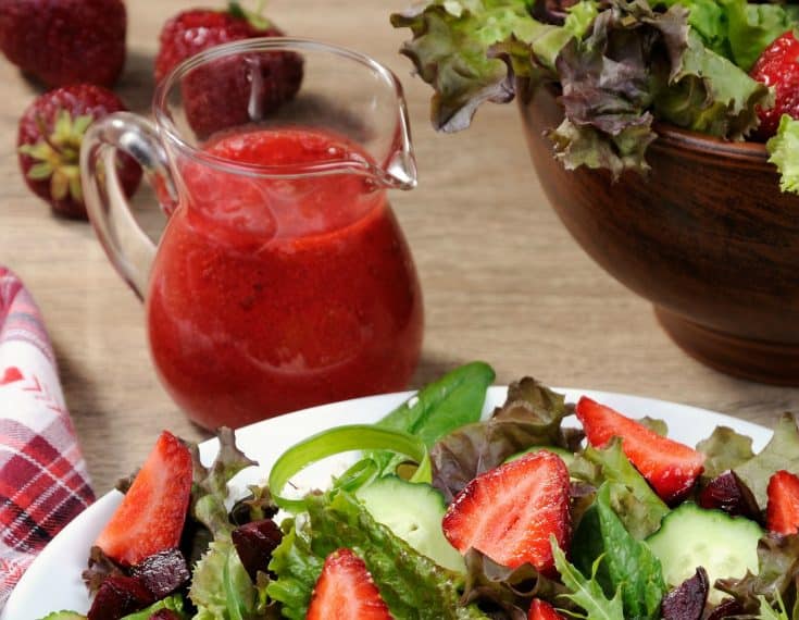 Salad on white dish and strawberry vinaigrette in small pitcher