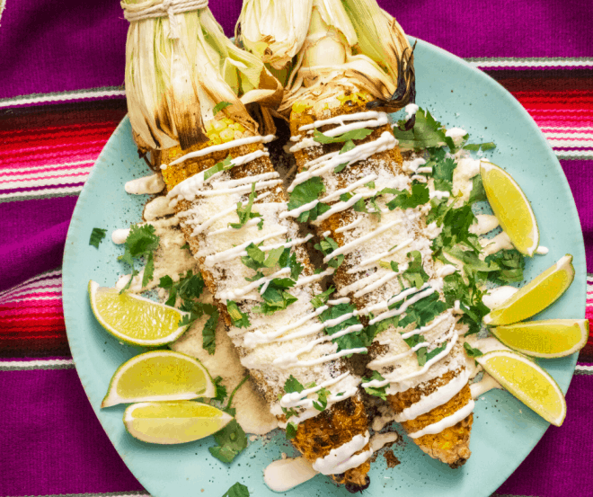 Mexican Street Corn on blue plate with limes and sour cream mixture