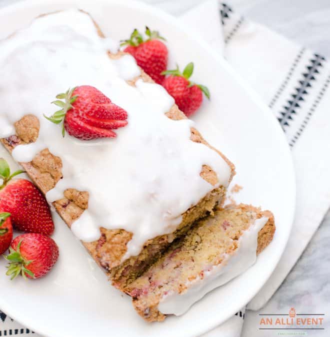 A loaf of strawberry bread with a white glaze on a white platter - garnished with fresh strawberries