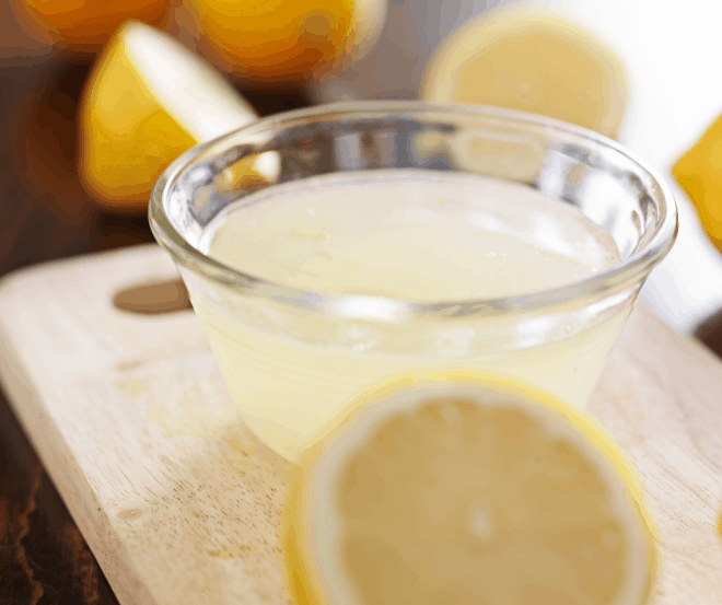glass cup of lemon juice surrounded by lemons