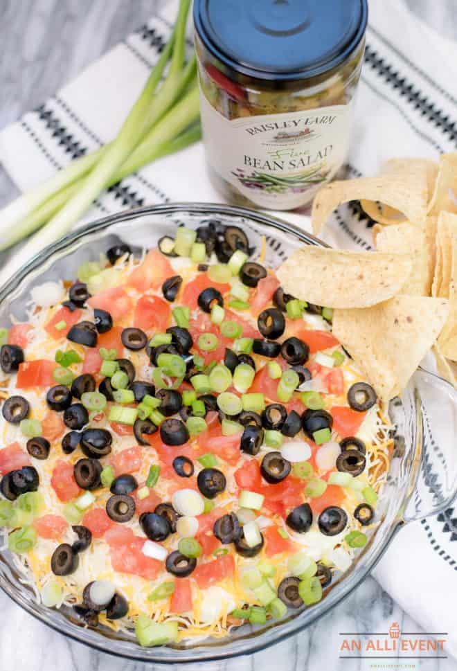 Bean Salad Taco Dip in a glass plate topped with chopped tomatoes and sliced black olives