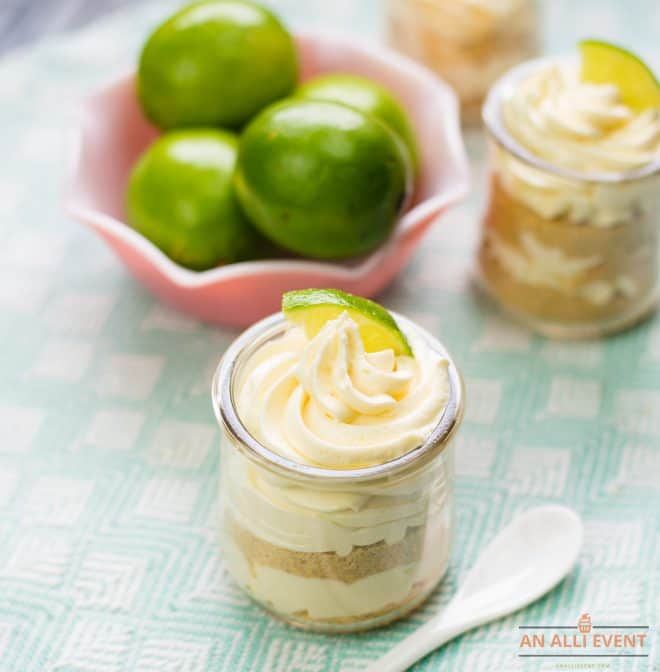 Layered Lime Cheesecake Pudding Parfaits in front of limes in pink bowl