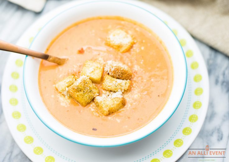 tomato soup in white bowl, topped with croutons and grated parmesan cheese