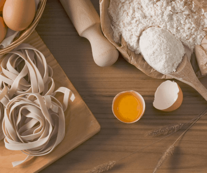 Making pasta - flour, rolling pin and pasta on brown cutting board