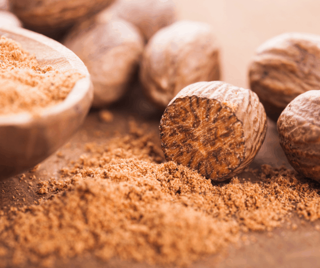 whole nutmeg and ground nutmeg on brown cutting board