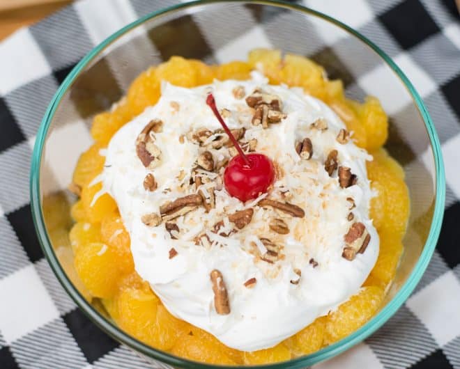 Old Fashioned Ambrosia - layer of orange segments, whipped cream, coconut, pecans and a cherry in a glass bowl