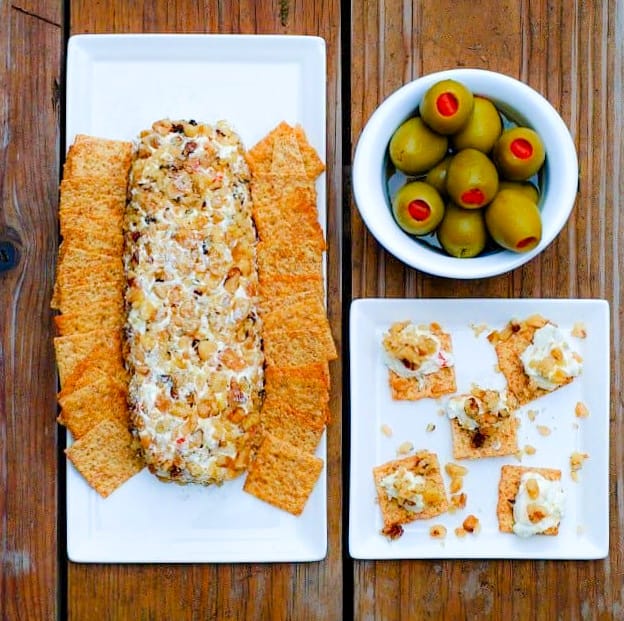 Walnut Olive Cheese Log on white serving platter surrounded by crackers and a bowl of Spanish olives