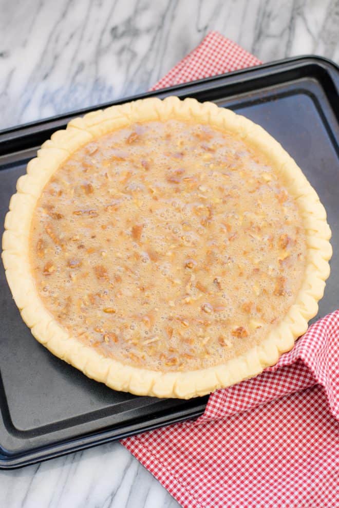 caramel pecan pie filling in pie shell before baking, placed on a dark brown cookie sheet