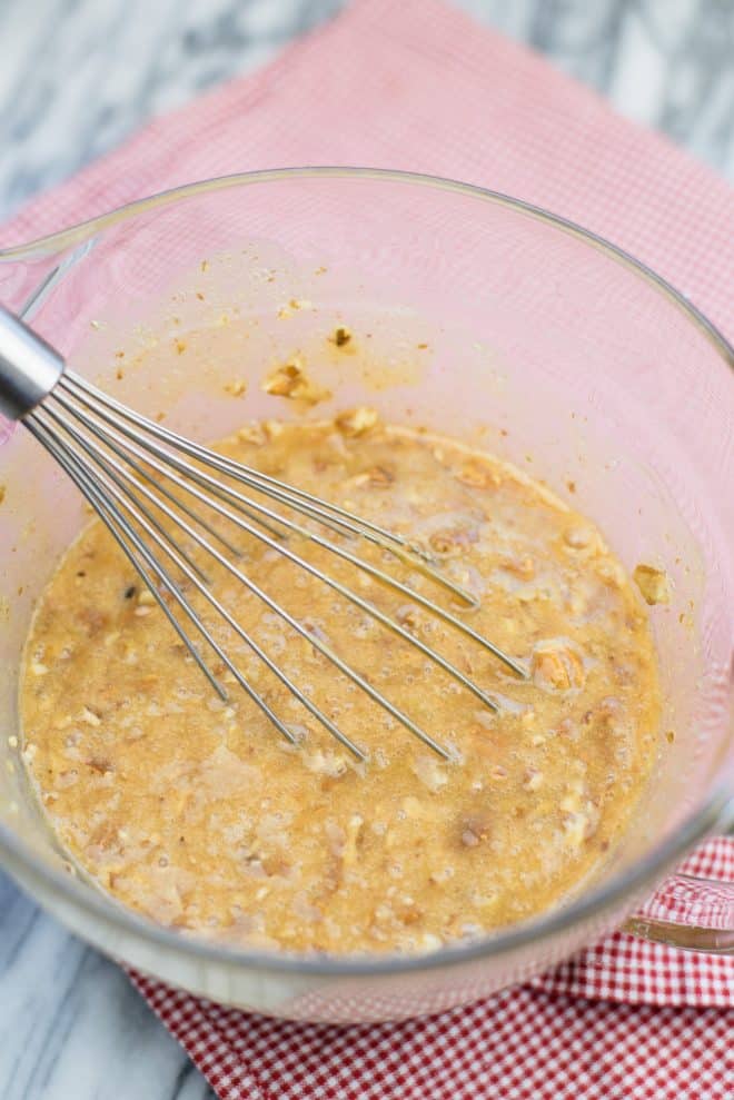 caramel pecan pie filling whisked together in a glass bowl on top of a red checked dishtowel 