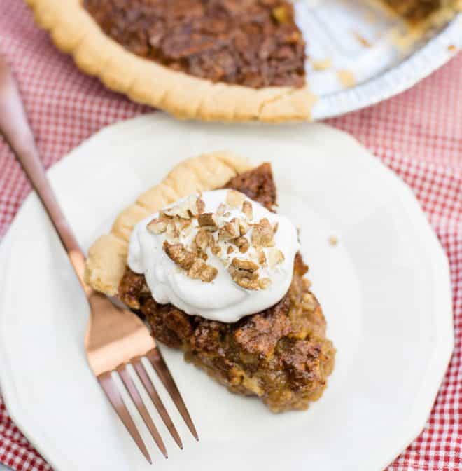 Slice of Caramel Pecan Pie on white serving plate with rose gold fork and whole pie in the background