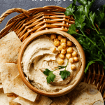 Brown woven tray holding a bowl of hummus and pita chips