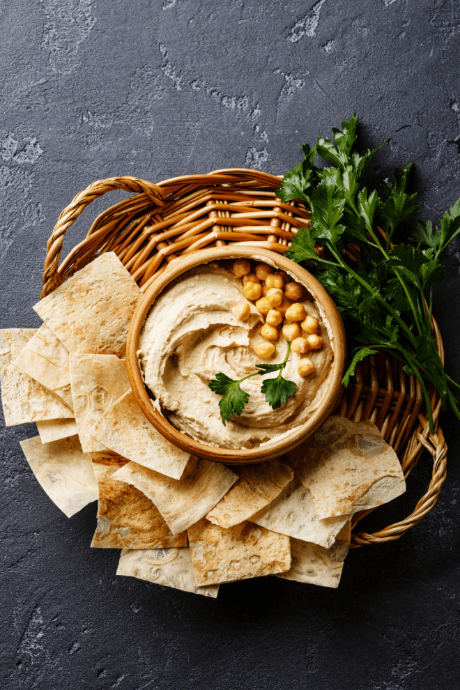 A bowl of easy homemade hummus in a brown basket surrounded by toasted pita chips