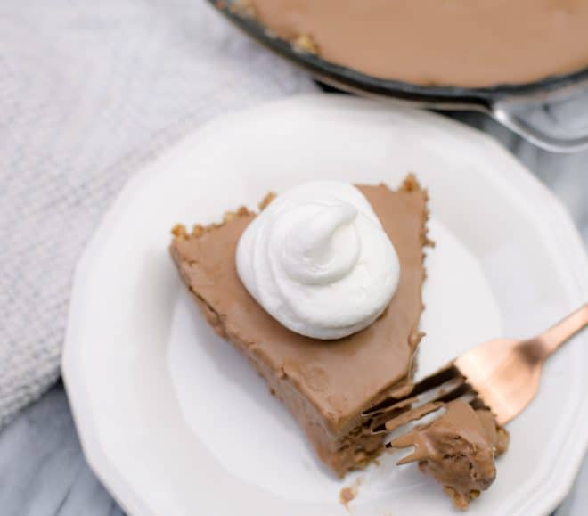 A closeup photo of a slice of chocolate pie on a white serving plate with a rose gold fork