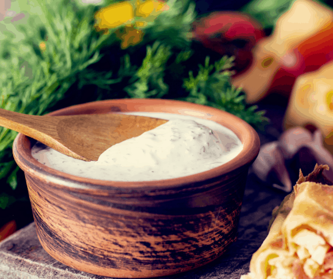 Tiger Dill Sauce in a brown bowl with a brown spoon with dresh dill and vegetables in the background