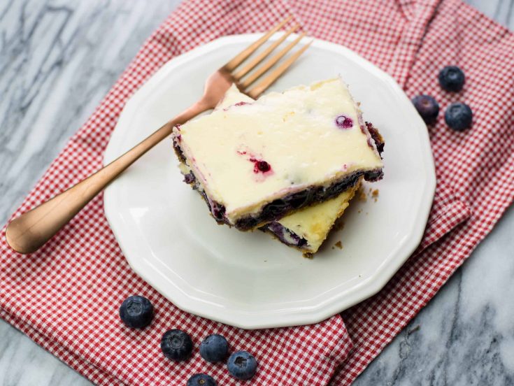 Blueberry Cheesecake Bars stacked on a small white plate on a red checked cloth