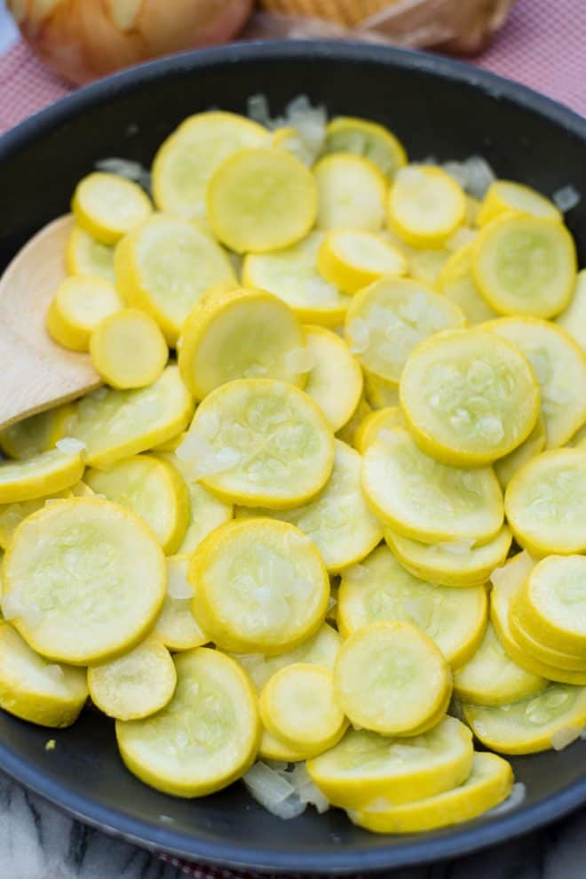 thinly sliced yellow squash with chopped onions in a skillet