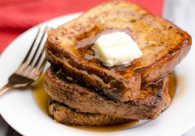 3 slices of Stuffed French Toast stacked on a white plate with a pat of butter and syrup