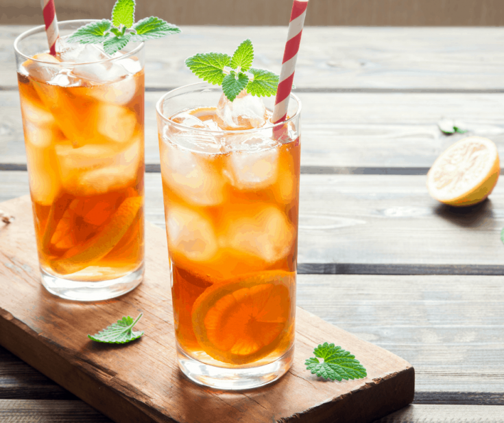 two glasses of sweet tea over ice on a wooden table. The glasses of iced tea are garnished with lemon slices and mint leaves