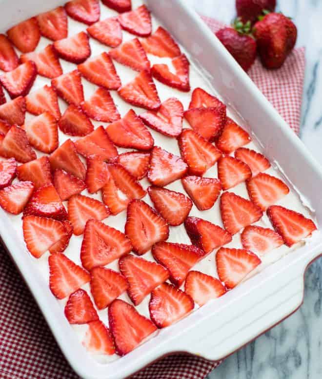 sliced strawberries on top of a cream cheese mixture in a oblong baking pan