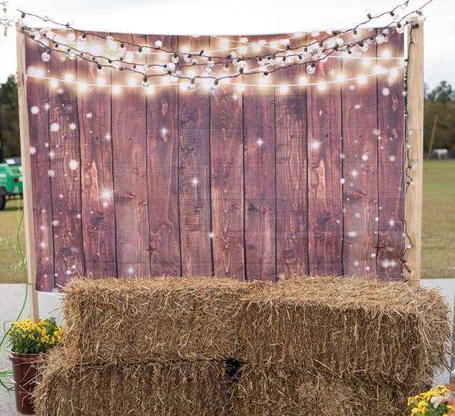 trunk or treat photo booth with string lights, wood plank backdrop and hay bales to sit on