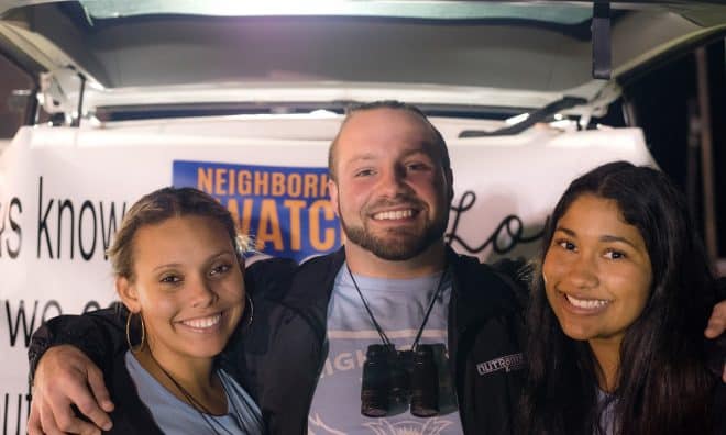 two girls and a boy smiling in front of a love your neighbor sign