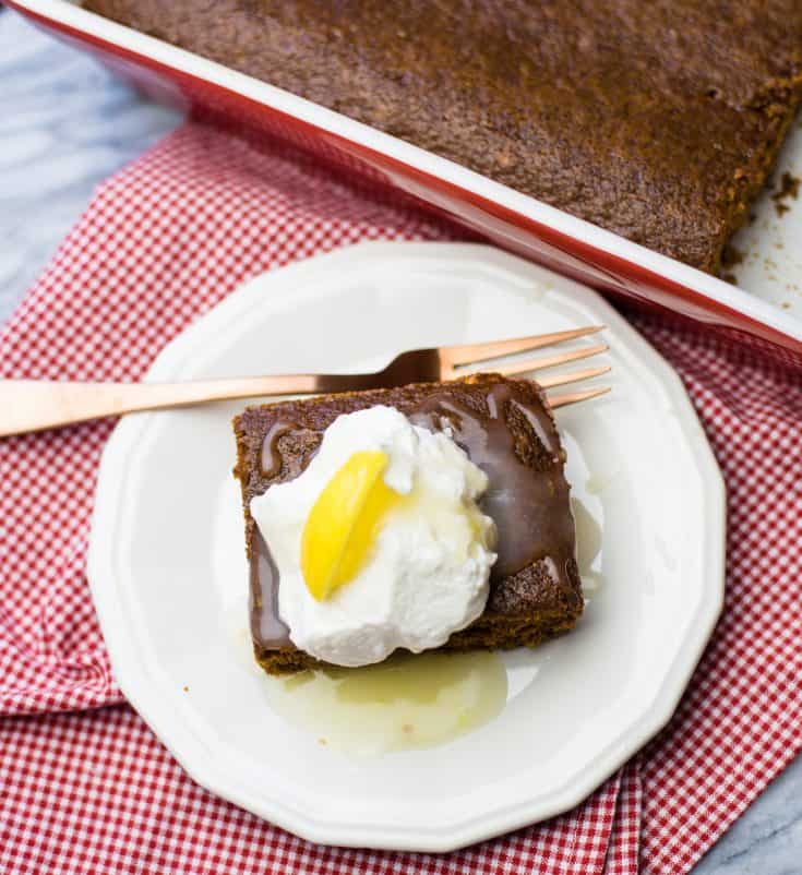 easy gingerbread in a 13x9 pan beside a white dessert plate with a square of gingerbread topped with lemon sauce and whipped cream