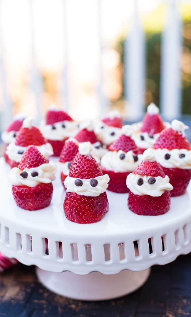 strawberries and cream strawberries that look like mini santa clauses on a white cake plate
