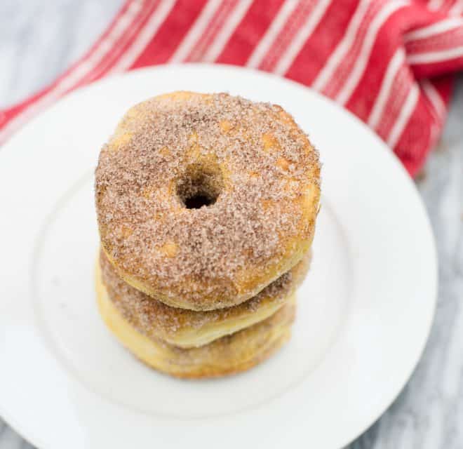 Cinnamon Sugar Doughnuts stacked on a white plate with a red and white dish towel in the background