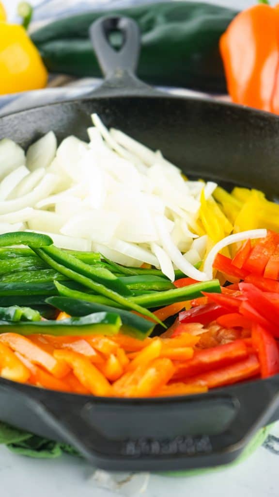 strips of peppers and onions cooking in a black cast iron skillet