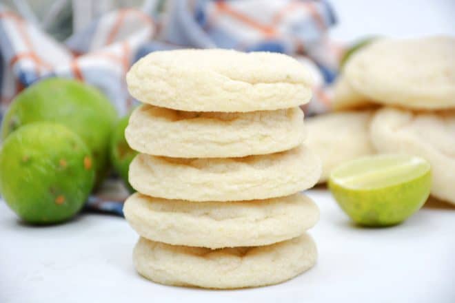 homemade key lime sugar cookies stacked up on top of each other with limes in the background