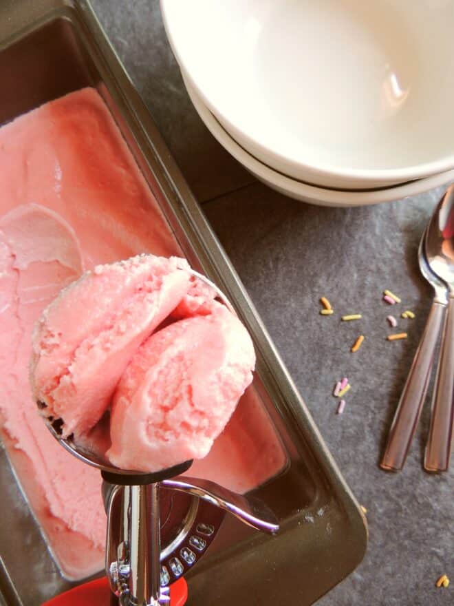 watermelon ice cream being scooped out of loaf pan