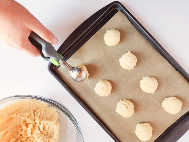 scooping sugar cookie dough onto parchment lined baking pan