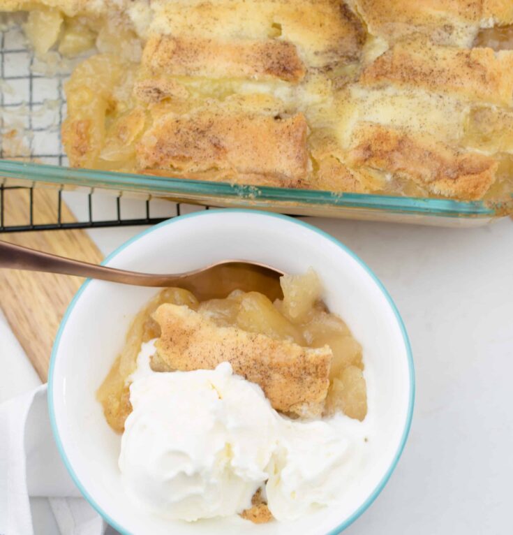 apple cobbler in a serving bowl in front of the 9x13 pan of apple cobbler