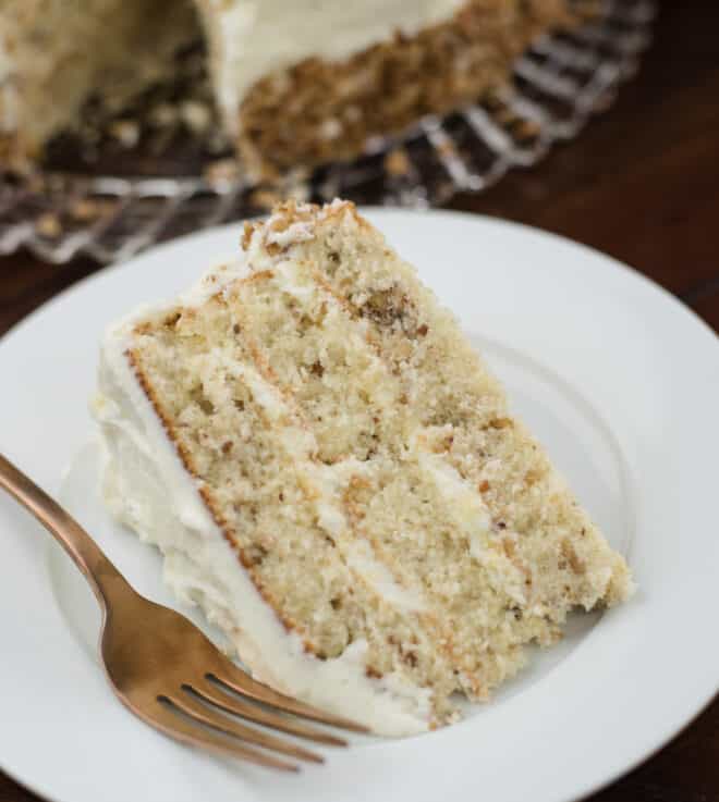 one slice of butter pecan cake on a white dessert plate with a rose gold fork