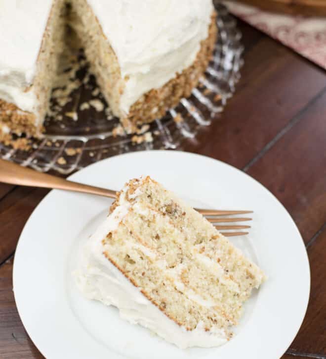 Slice of butter pecan cake on a white dessert plate with the rest of the cake in the background
