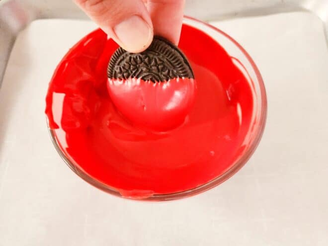 Oreo being dipped into melted red candy melts.