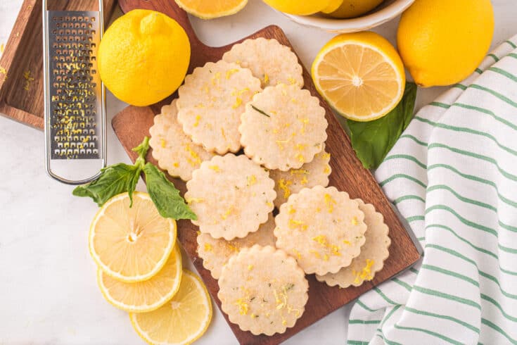 close up photo of lemon basil shortbread cookies surrounded by sliced lemons and fresh basil