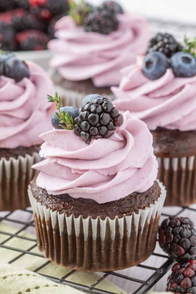 Chocolate Cupcakes topped with Blackberry buttercream and garnished with blackberries and blueberries placed on a cooling rack